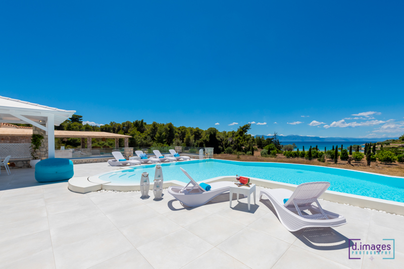 Φωτογράφιση βίλας, εξωτερική πισίνα με λευκές ξαπλώστρες, τιρκουάζ πισίνα και γαλάζιο ουρανό.